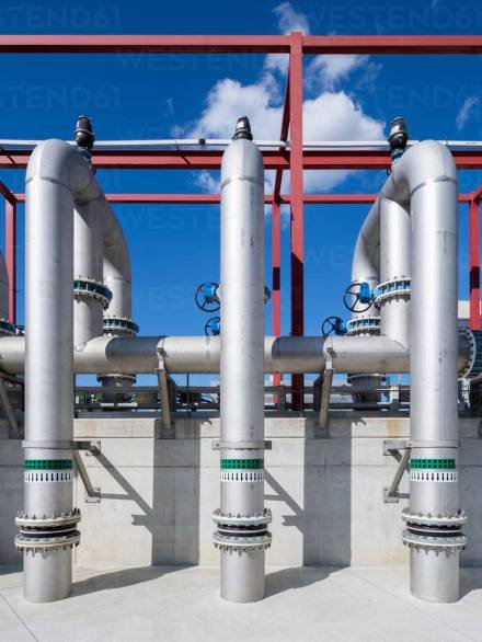 Modern exterior of construction of gray metal water pipes and tubes with circulation pumps and valves of industrial building against blue sky