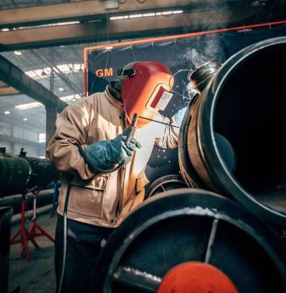 A vertical shot of a welder wearing a helmet and welding steel tubes in a factor